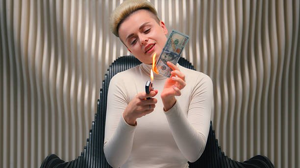 Caucasian businesswoman laughing wildly while burning cash, showing crazy and bizarre behavior.