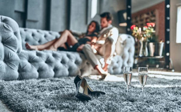 Stylish couple on sofa — bearded man in suit, woman in black dress at home. 📝 Description: