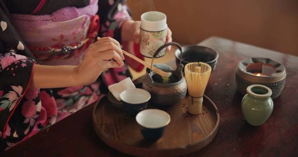 Japanese woman preparing matcha tea at home with teapot and herbs.