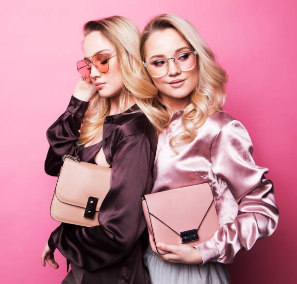 Two fashionable women pose with bags and sunglasses, showcasing designer dupes 2025.
