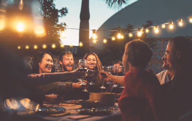 Happy multiethnic group enjoying barbecue dinner with red wine outdoors