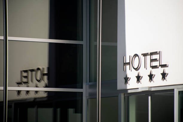 The modern exterior of a building with a sign featuring the word "HOTEL" in large, silver letters above four matching stars, indicating it is a 4-star hotel. The sign is reflected in the large glass windows of the building.