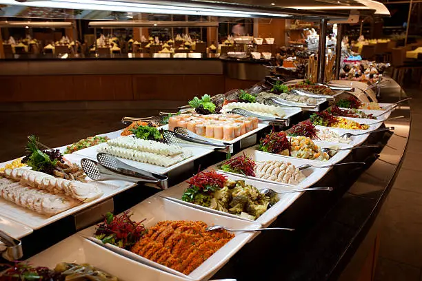 An abundant buffet spread showcasing budget-friendly buffet meal ideas, with a long line of white platters filled with salads, sliced meats, and other party foods.