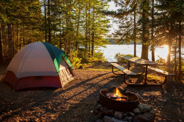 Campsite on lake in northern Minnesota with campfire at sunset A serene lakeside campsite with a tent, picnic table, and a small campfire, perfect for cheap camping meal ideas.
