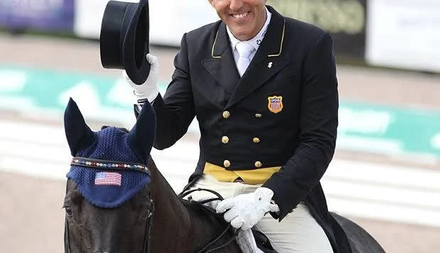 A smiling Cesar Parra in a US Equestrian team coat tips his top hat while on horseback, an image highlighting the professional persona discussed in the context of Cesar Parra and Budget-Rider ethics.