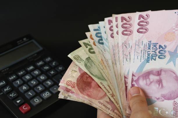 A person holding a stack of Turkish banknotes in front of a calculator, illustrating practical ways to save money.