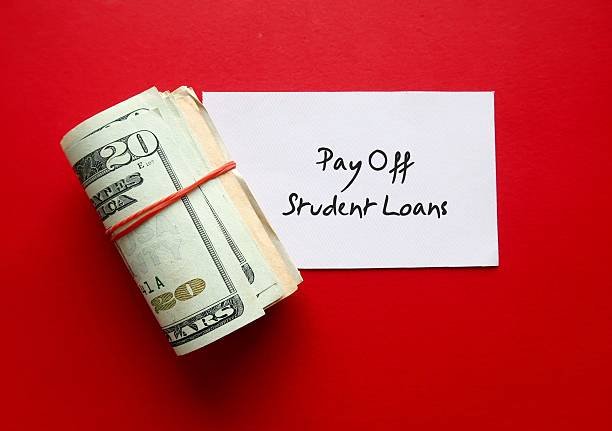 A roll of cash on a red background next to a white notecard that reads 'Pay Off Student Loans,' symbolizing a plan to pay off debt fast.