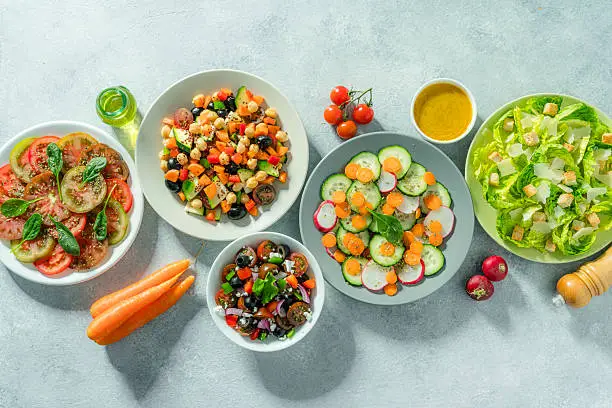 A top-down view of several plates and bowls filled with colorful, fresh summer salads, representing affordable and delicious budget summer meals for entertaining.
