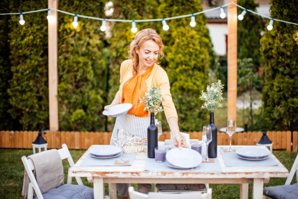 A host setting a beautiful outdoor table under string lights, preparing to serve easy party meal ideas to her guests.