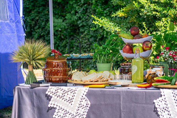 summer party A rustic buffet table at an outdoor event, offering inspiration for Summer Dinner Party Themes with its spread of fresh fruit, sliced bread, homemade preserves, and drinks under a canopy.