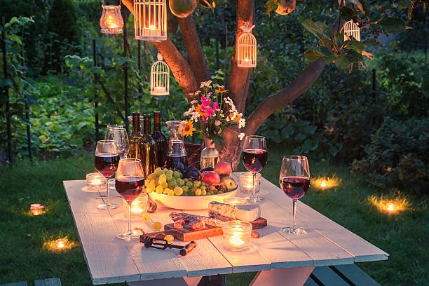 Outdoor dinner table with wine, cheese, fruit, and lanterns in a garden at dusk.
