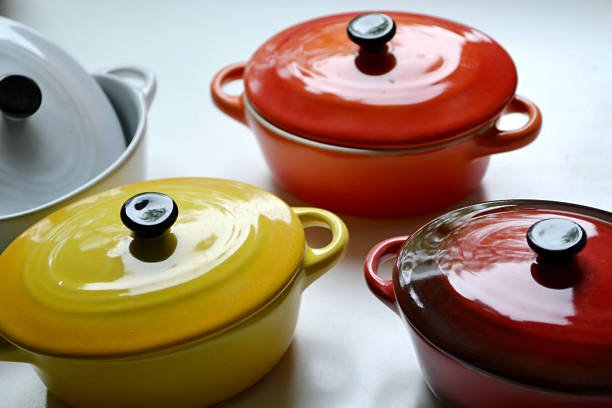Colorful Le Creuset dupes, including yellow, red, white, and orange enameled cast iron Dutch ovens, displayed on a white surface.