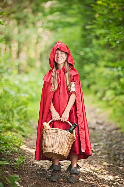 Little Red Riding Hood standing on the forest path. Slightly soft. A happy child dressed in a red hooded cape and carrying a basket, showcasing a classic Little Red Riding Hood DIY Halloween costumes
