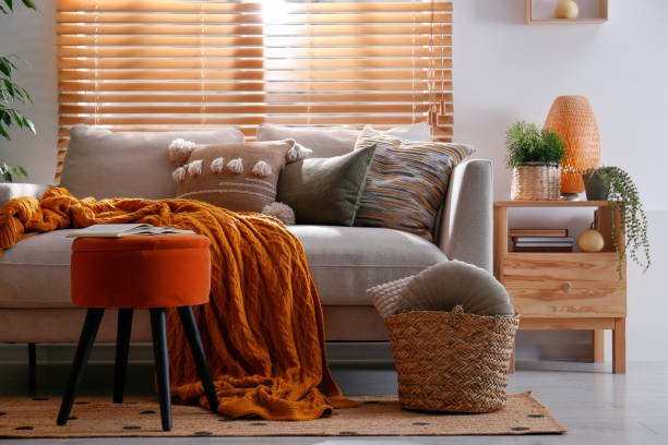 Cozy fall living room decor featuring a sofa with a chunky orange throw blanket, textured pillows, and a woven basket, creating a warm and inviting autumn atmosphere.
