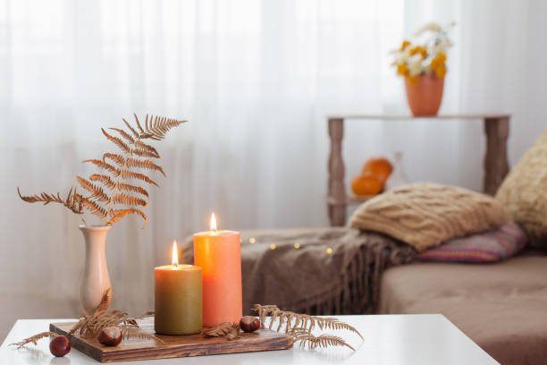 burning candles with autumn decor on white table at home home decor