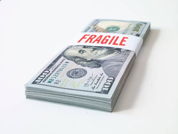A crumpled US dollar bill stamped with the word "FRAGILE," visually illustrating cash erosion and the need for a  resilient-emergency-fund-2025-volatile-economy