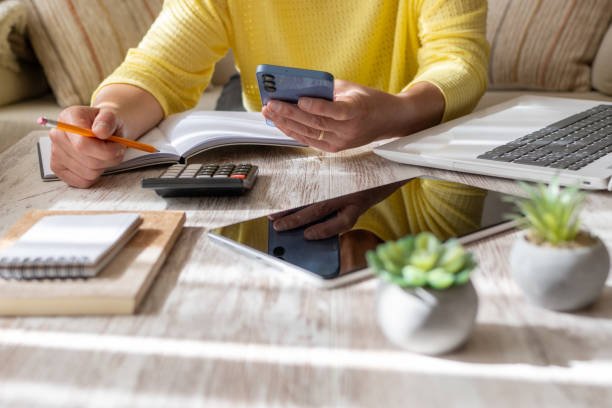 Budgeting in 2025: A person using a calculator and smartphone to manage personal finance, with a laptop and notebook visible on a desk, representing modern adaptive budgeting.