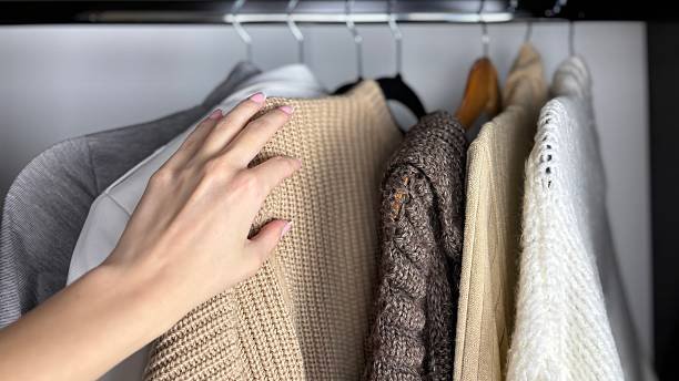 A hand is organizing the cloths in wardrobe, showcasing fall wardrobe organization.