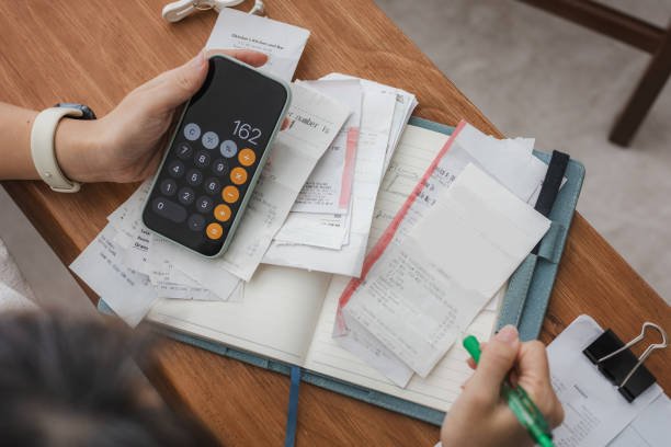Budgeting in 2025: Close-up of hands holding a pencil and smartphone over a calculator and financial planner, illustrating money-saving tips and smart spending in the 2025 economy.
